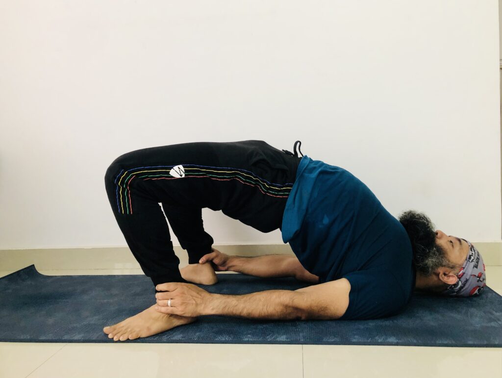 A man performing the downward dog yoga pose on a mat, showcasing flexibility and balance in Sethu Bandhasana.
